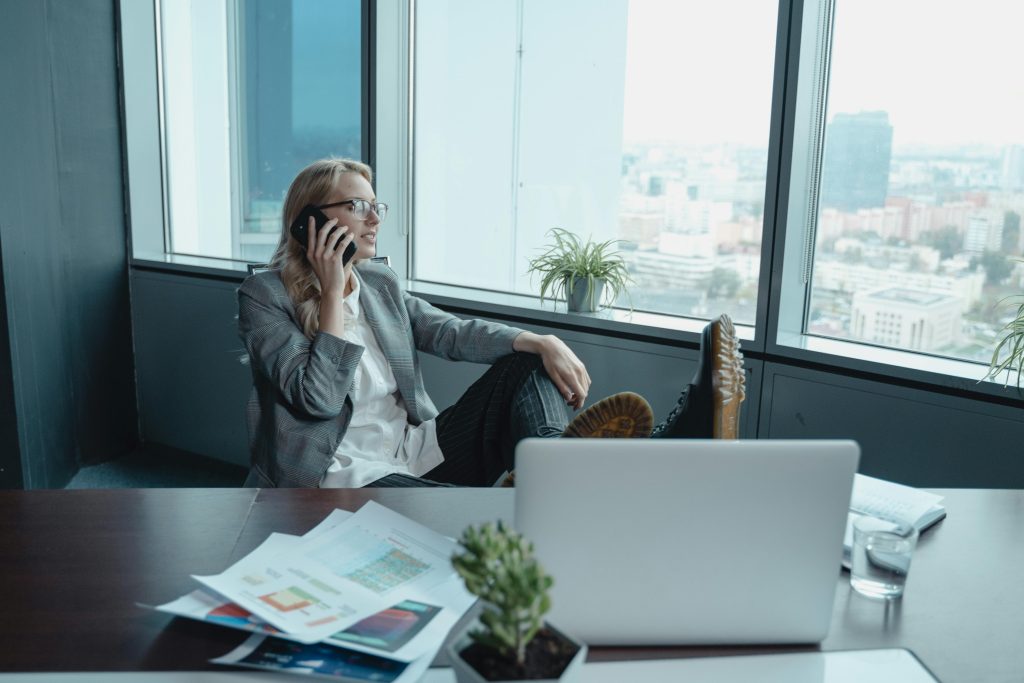 A businesswoman in gray coat sitting on a swivel chair while talking on the phone