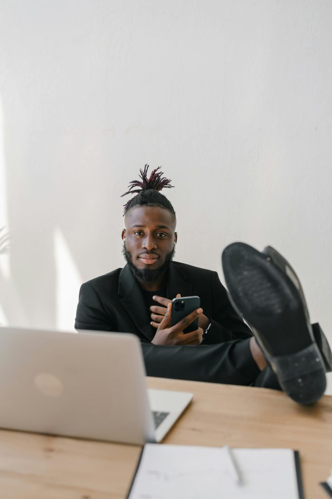 A businessman in Black Suit with his Legs Up on the Table looking very relaxed